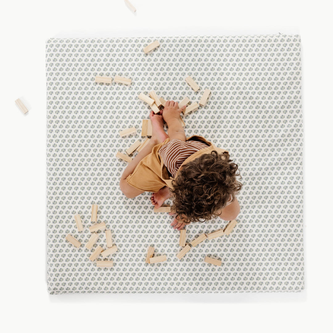 Blue floral block-print padded baby play mat, overhead view with a toddler and wooden blocks.