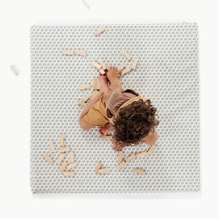 Blue floral block-print padded baby play mat, overhead view with a toddler and wooden blocks.