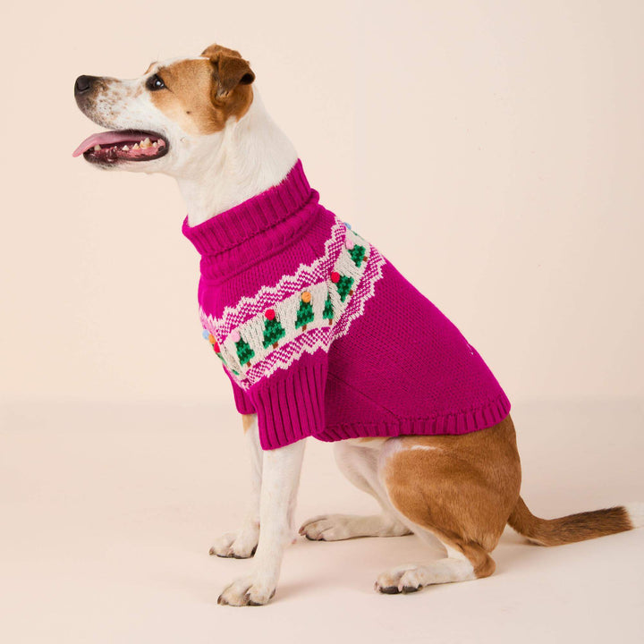 Side view of a seated brown-and-white dog in a magenta turtleneck Christmas sweater.