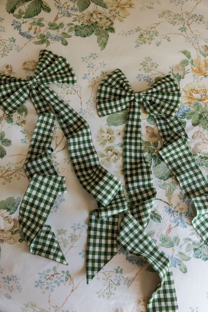 Several hunter green gingham fabric bows arranged against floral wallpaper