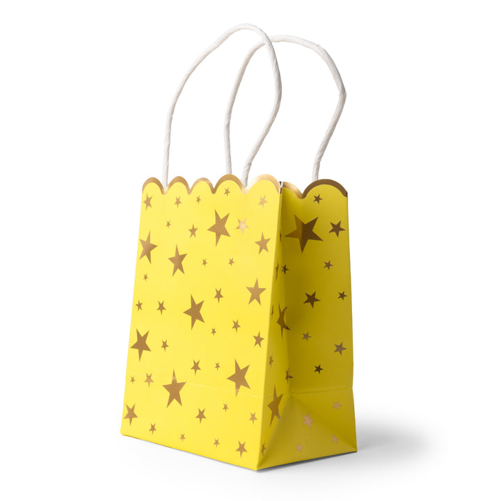 A small yellow paper party bag with a scalloped top edge, decorated with metallic gold stars of various sizes, and finished with white twisted paper handles, shown on a white background.