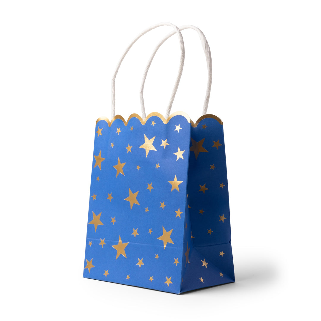 A blue paper gift bag with a scalloped top edge, decorated with gold stars of various sizes, and featuring two white paper handles on a white background.