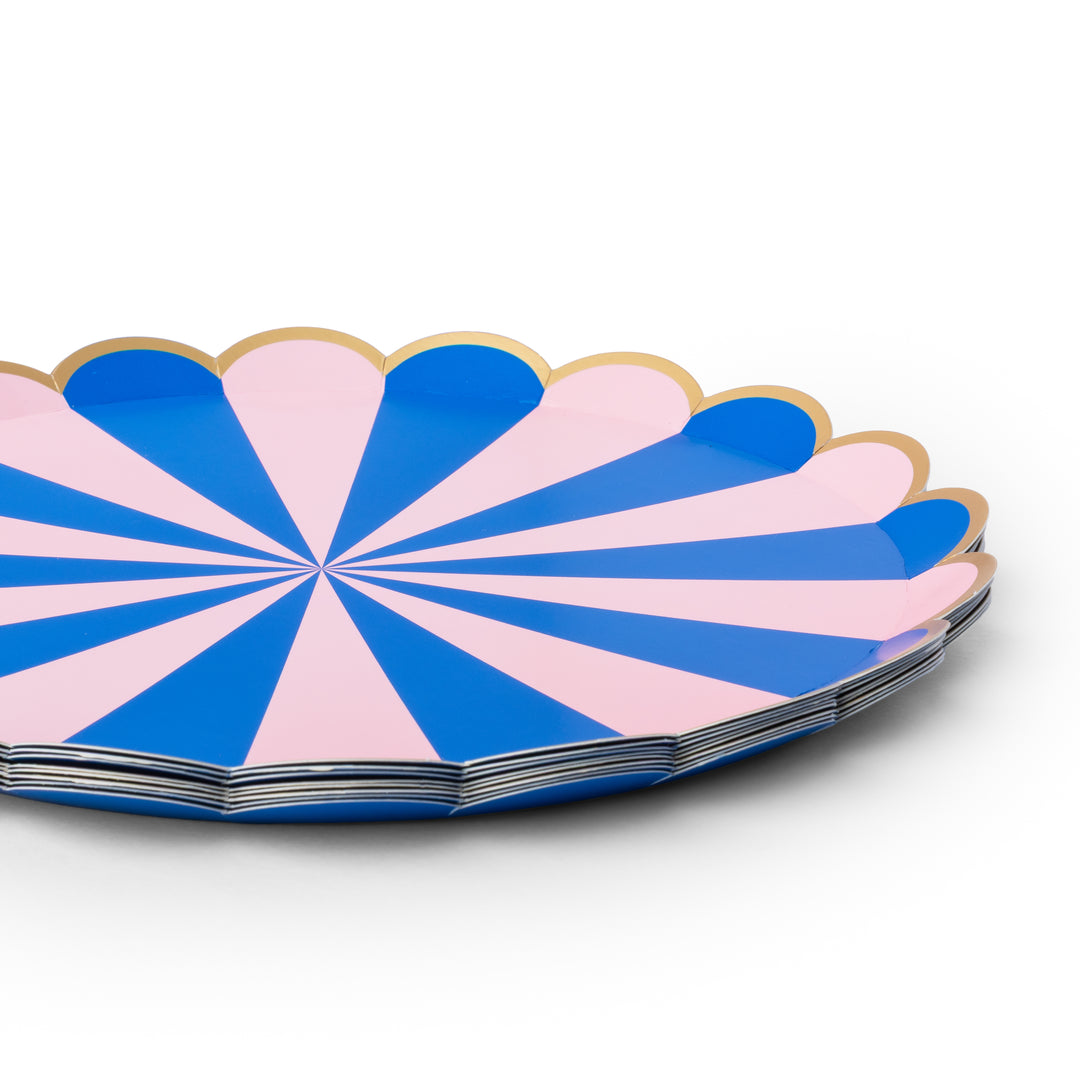 A stack of scalloped paper plates with a blue and pink radial striped pattern and a thin gold rim, photographed on a clean white background.
