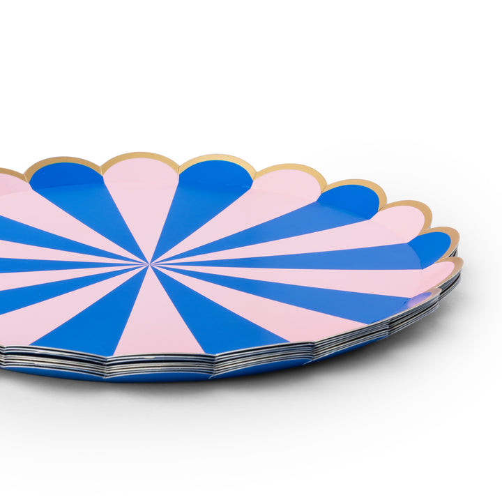 A stack of scalloped paper plates with a blue and pink radial striped pattern and a thin gold rim, photographed on a clean white background.