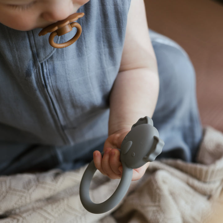 Close-up of a baby holding a grey Mushie koala ring teether