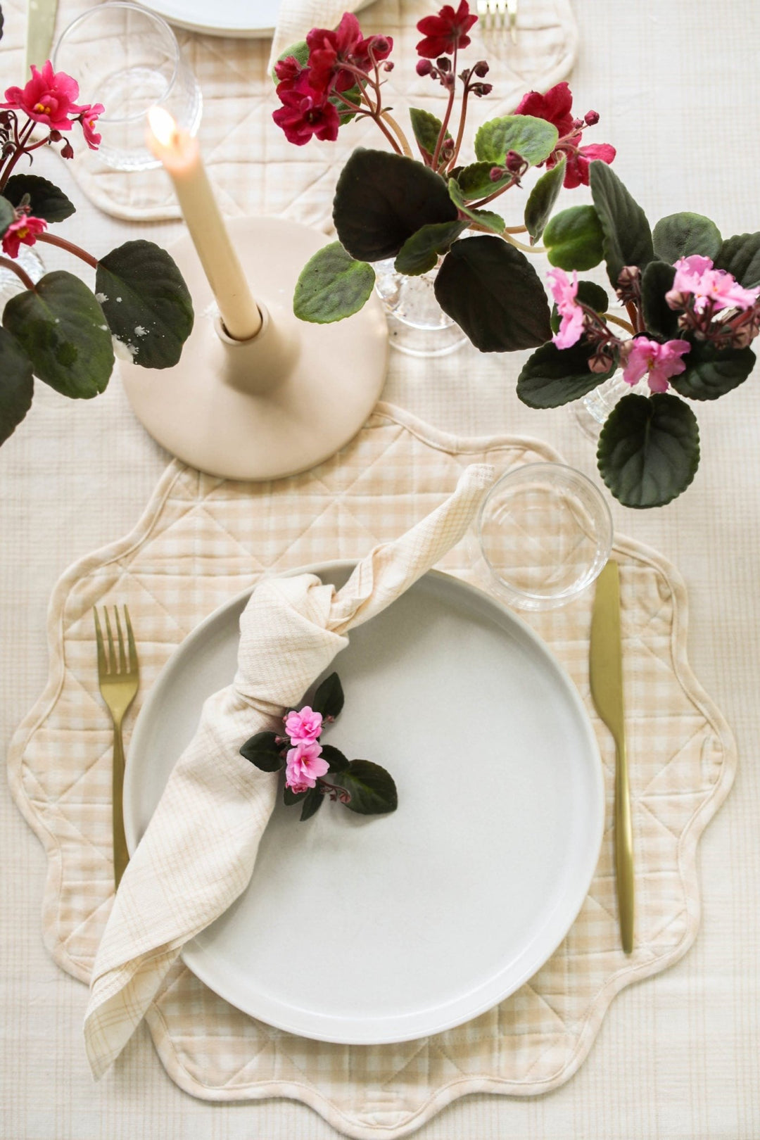 Cream plaid napkin at a spring place setting with a white plate, taper candle, and cyclamen
