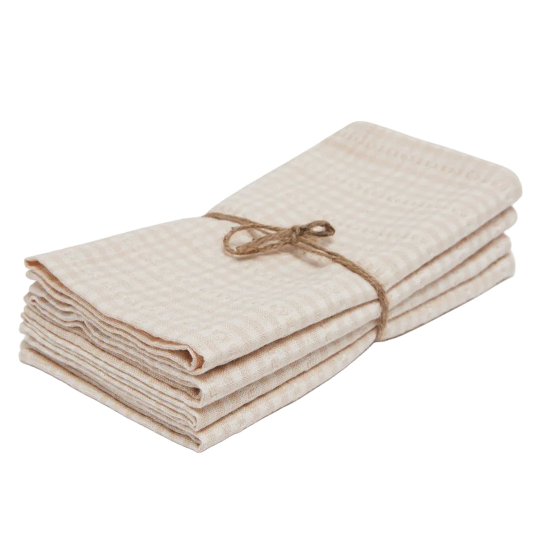 A stack of folded cotton muslin cloths in a beige and white gingham pattern, tied with a natural jute twine bow, on a light gray background.