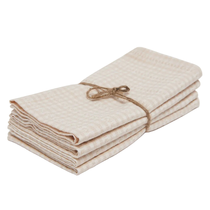 A stack of folded cotton muslin cloths in a beige and white gingham pattern, tied with a natural jute twine bow, on a light gray background.