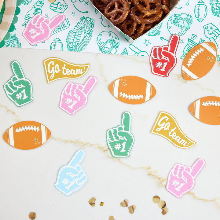 Foam finger, football, and pennant jumbo confetti scattered on a marble table with gold dots