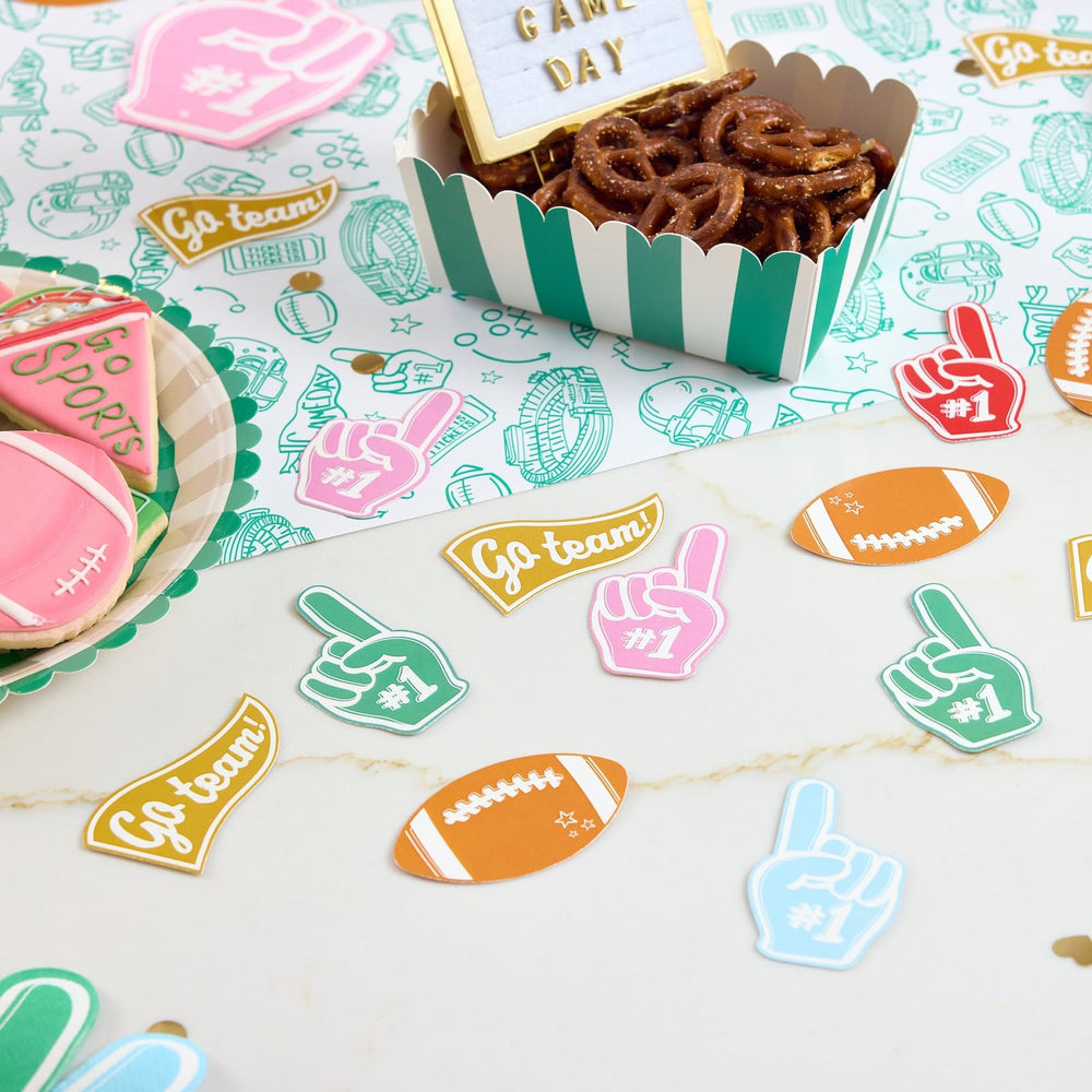 Jumbo football confetti scattered on a table beside a snack box of pretzels
