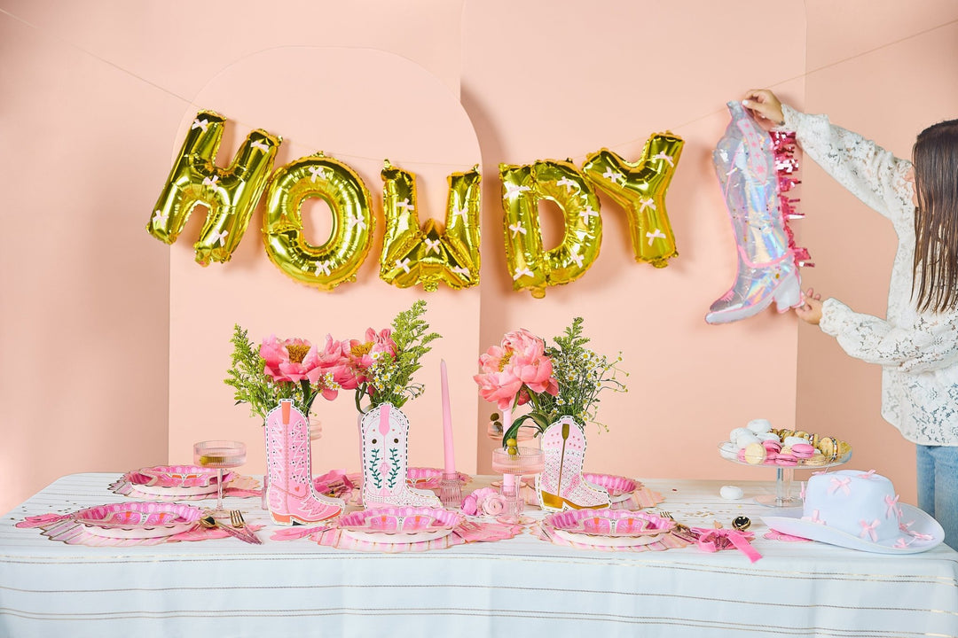 Gold balloon letter banner spelling Howdy Darling, tied with pink satin bows