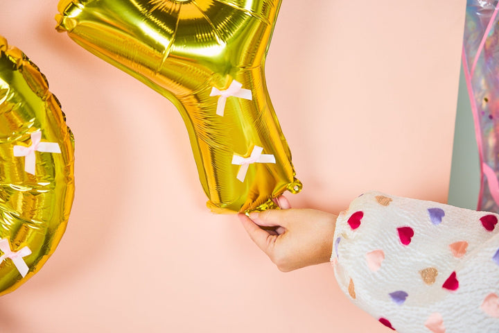 Gold balloon letter banner spelling Howdy Darling, tied with pink satin bows