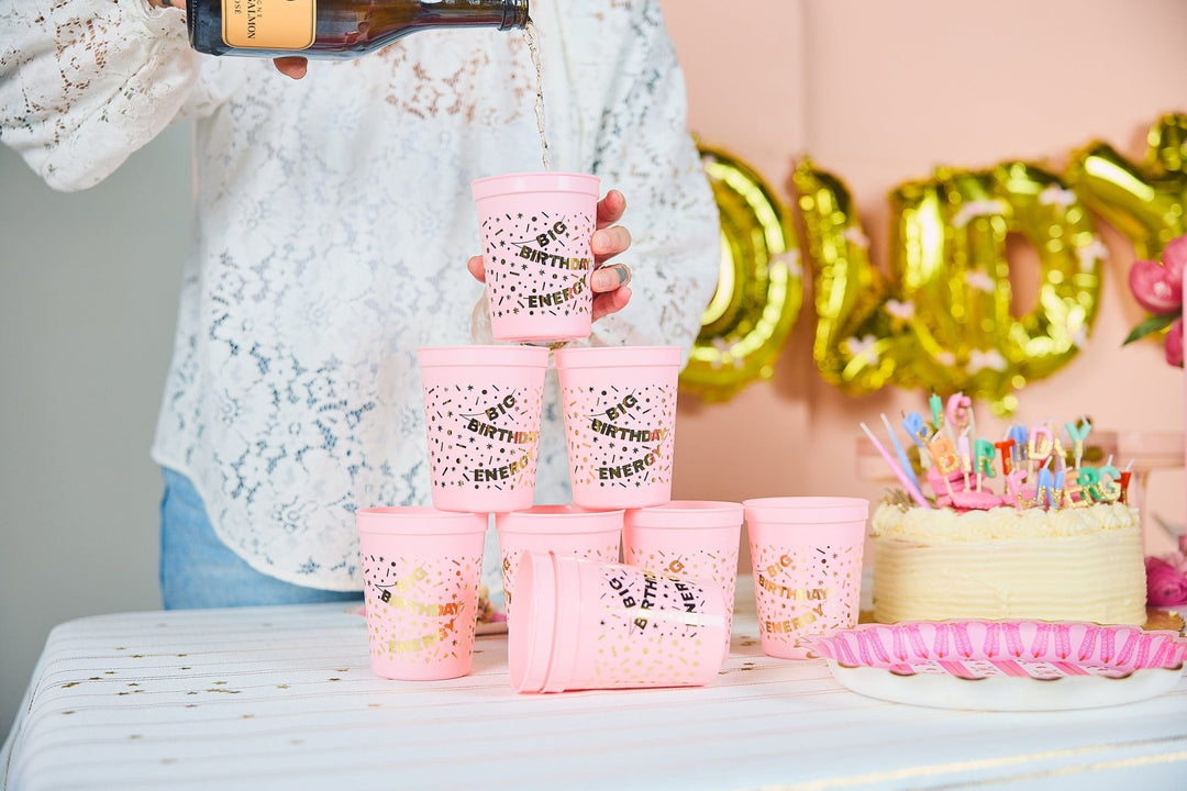 Bubbly poured into a tower of pink Big Birthday Energy cups beside a birthday cake