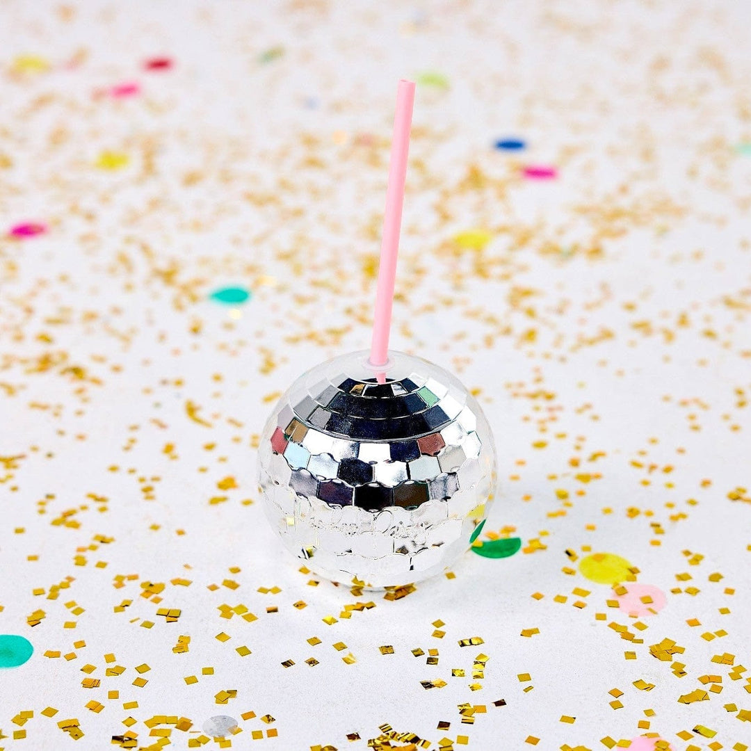 Silver disco ball cup with a pink straw on a white table scattered with gold and pastel confetti