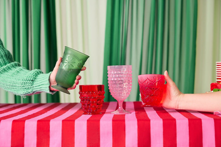 Hands setting green, red, and pink vintage-style cups on a red and pink striped tablecloth