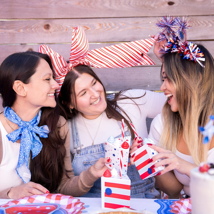 Three women laughing at a 4th of July party holding striped cake slice cups