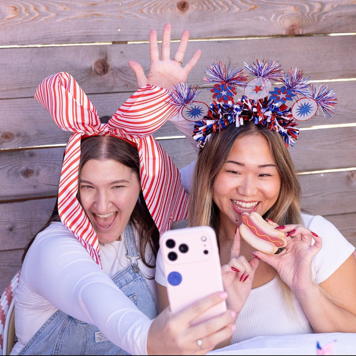 Two friends taking a selfie, one wearing the jumbo striped bow headband