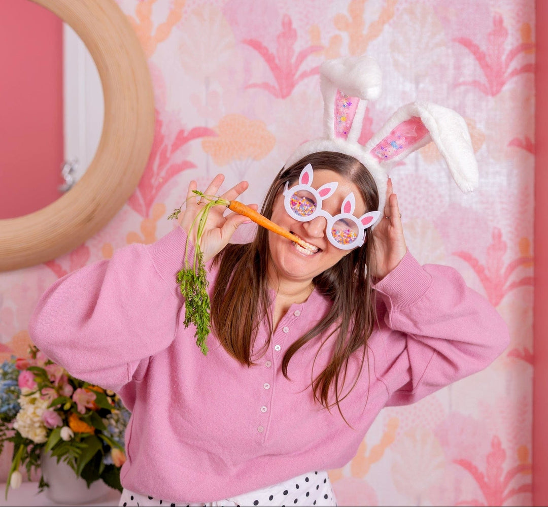 Woman in the plush bunny ears and bunny glasses holding a carrot to her face