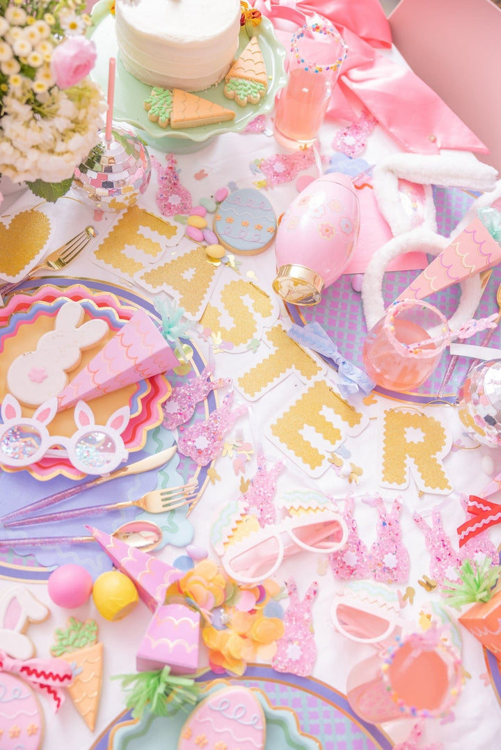 Easter party table with a gold Easter balloon banner, bunny plates, and egg sippers