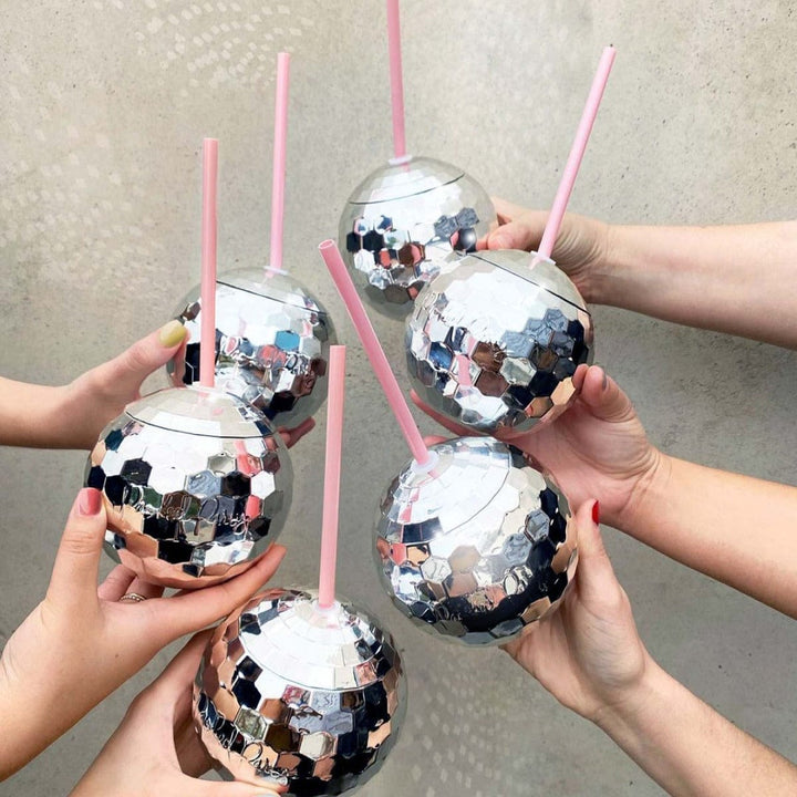 Group of hands raising silver disco ball cups with pink straws in a toast
