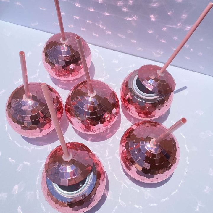 Six pink disco ball cups with straws casting sparkles on a white tabletop