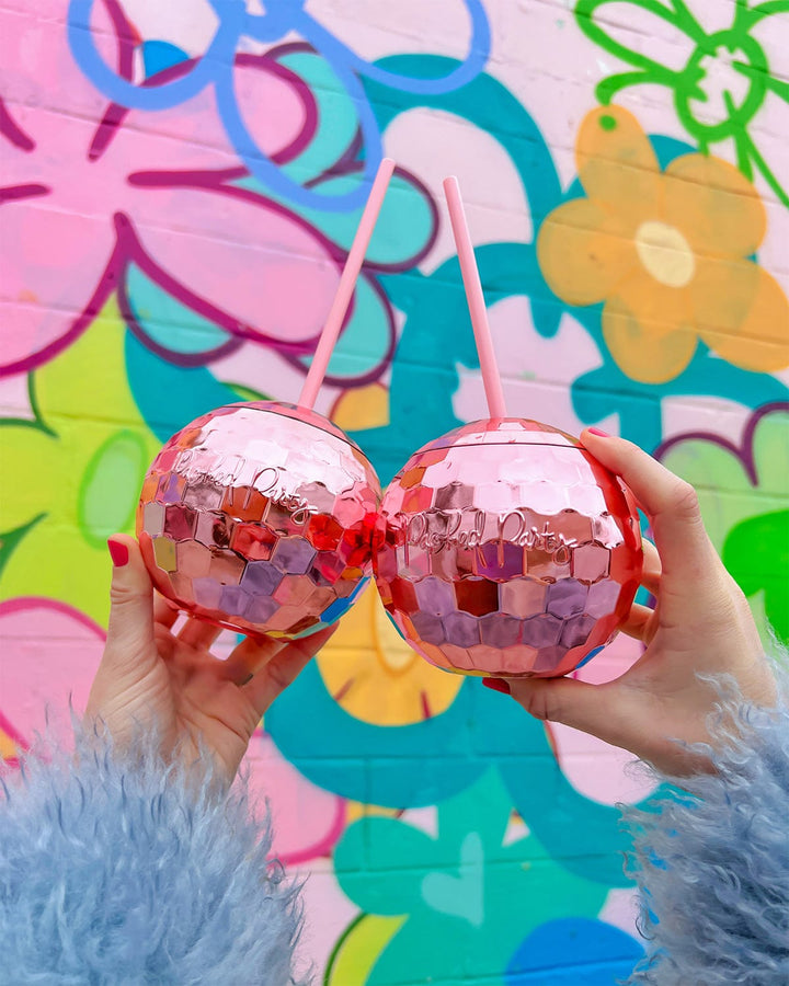 Two hands holding pink disco ball cups against a colorful flower mural