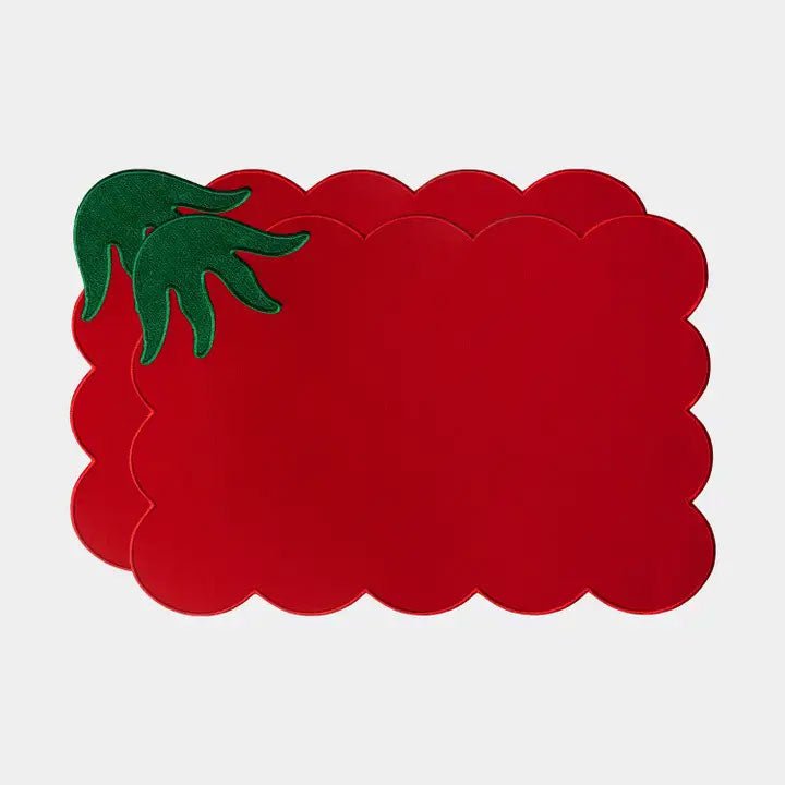 Red scalloped placemats shaped like a tomato with a green leafy stem, stacked on a light gray backdrop