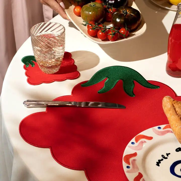 Tomato placemat on a white tablecloth with a matching coaster, glassware, and bread, styled for an Italian dinner party