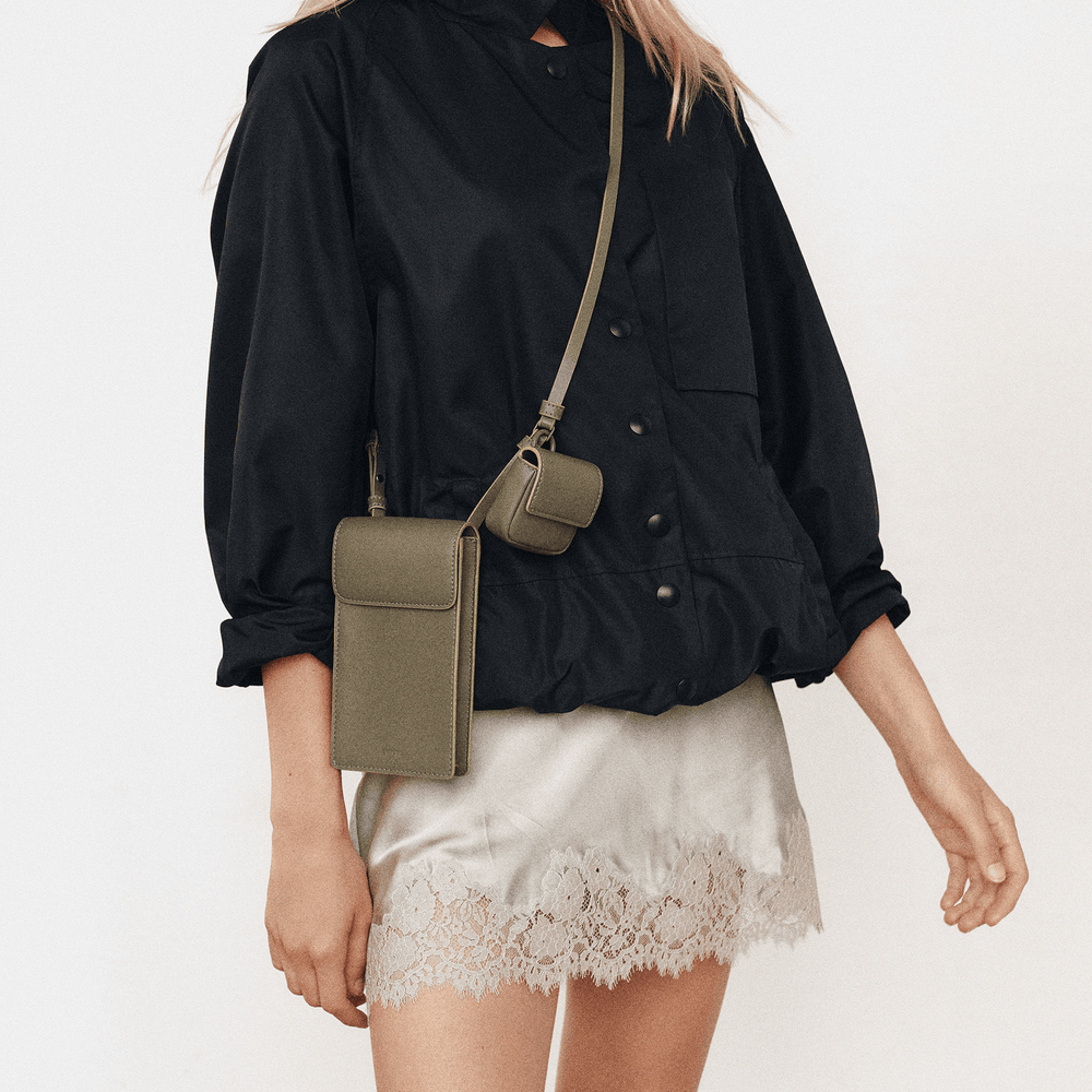 Model wearing the olive Georgia phone sling crossbody over a black shirt and lace slip skirt