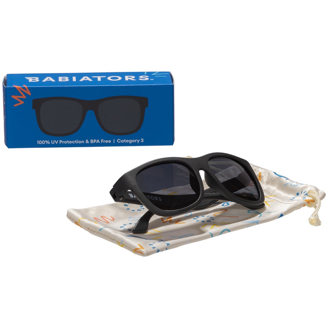 Black aviator kids sunglasses folded on a printed storage pouch beside the Babiators Originals box.