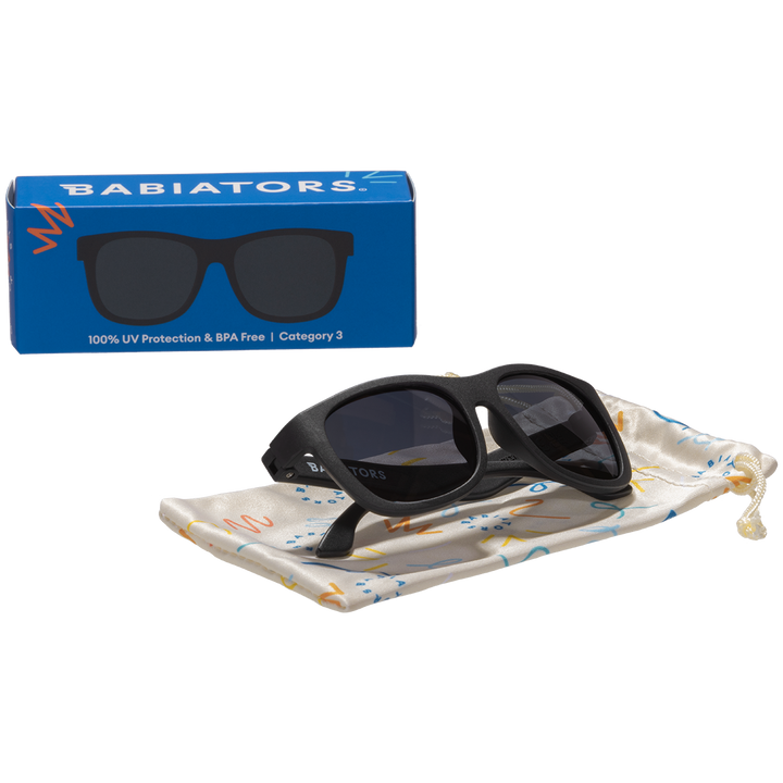 Black aviator kids sunglasses folded on a printed storage pouch beside the Babiators Originals box.