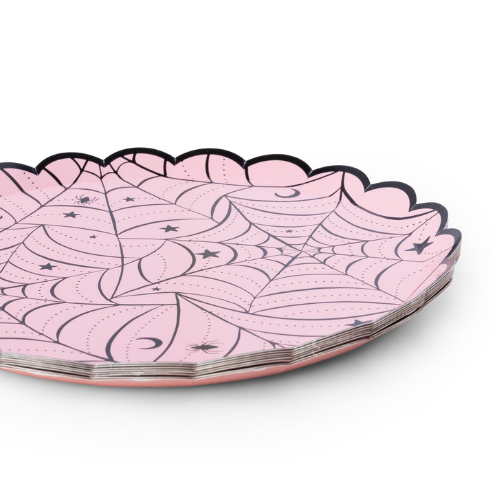 A stack of scalloped-edge paper plates in light pink, decorated with black spiderwebs, stars, and crescent moons, shown on a clean white background.