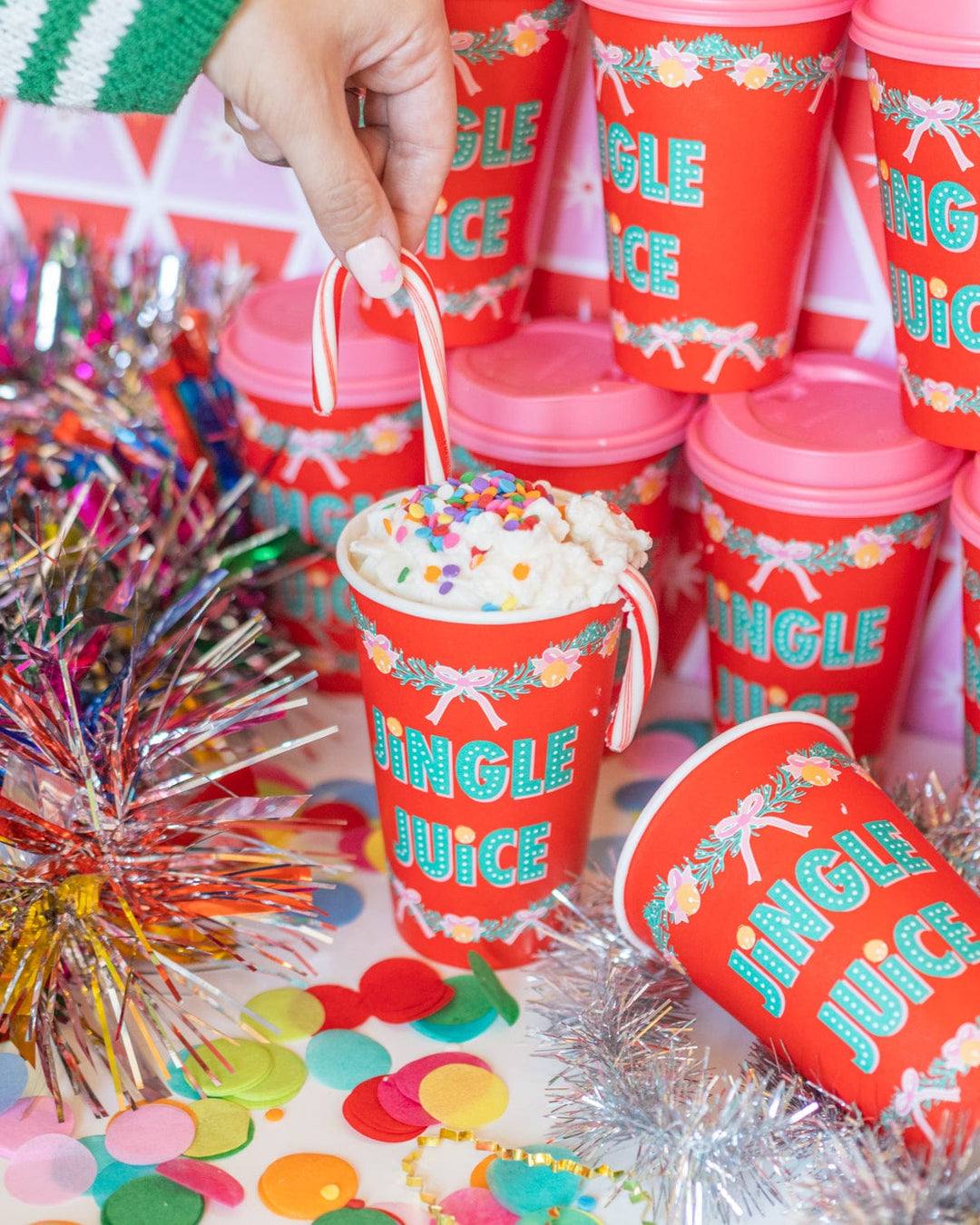 Hand dropping candy into a red Jingle Juice Christmas cup surrounded by cups and confetti