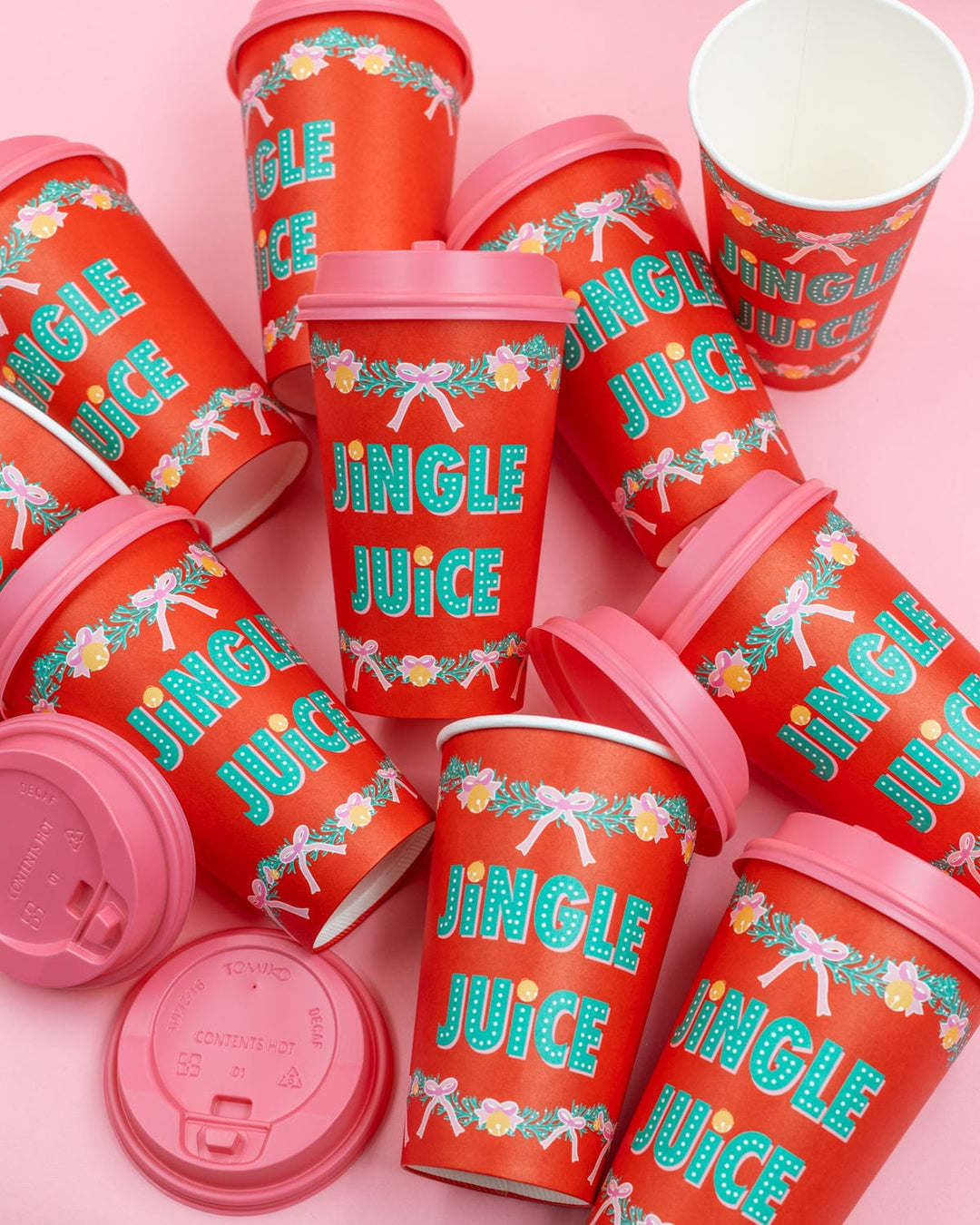 Ten red Jingle Juice Christmas cups with pink lids lined up on a pink background