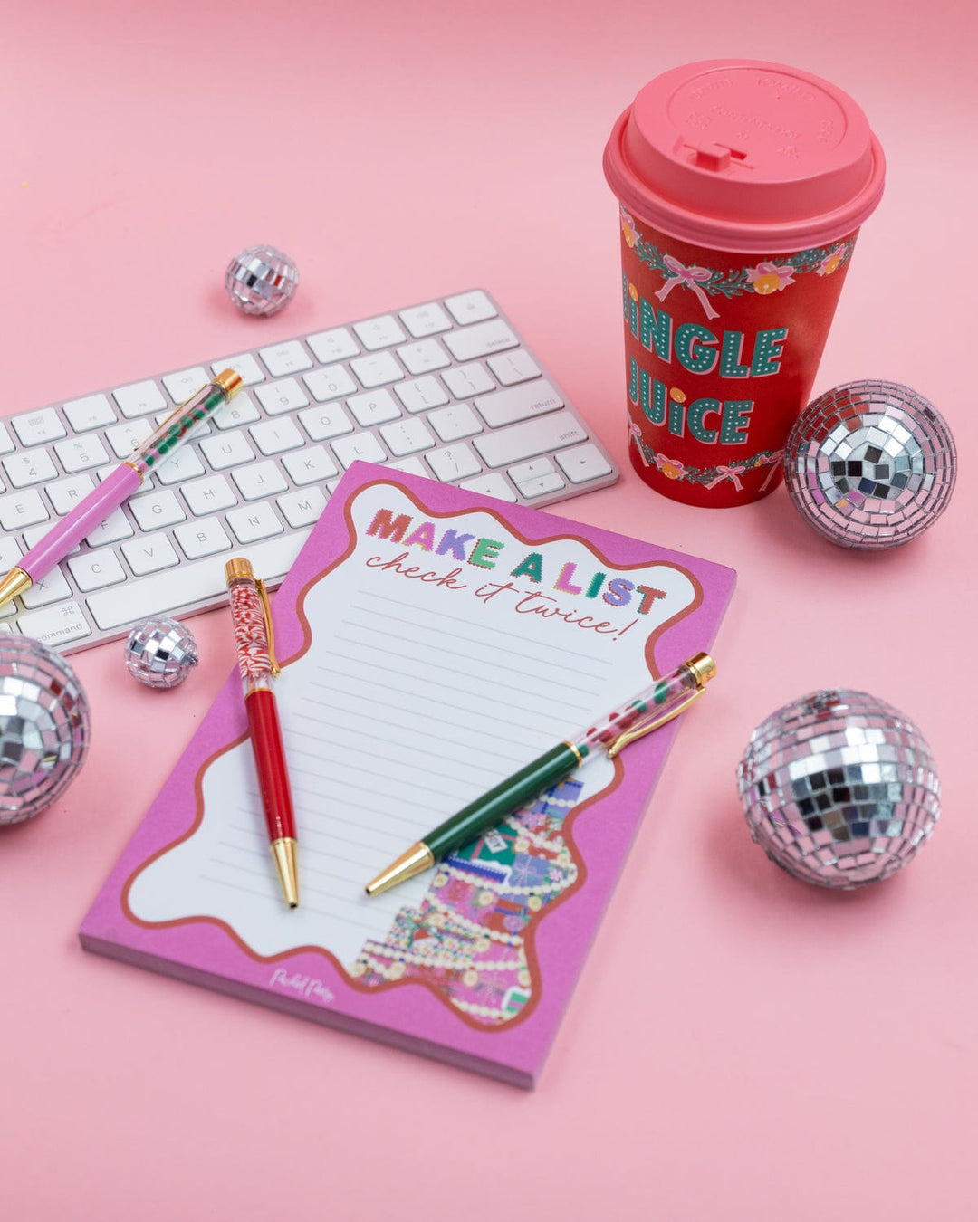 Red Jingle Juice Christmas coffee cup among desk supplies and disco balls on a pink background