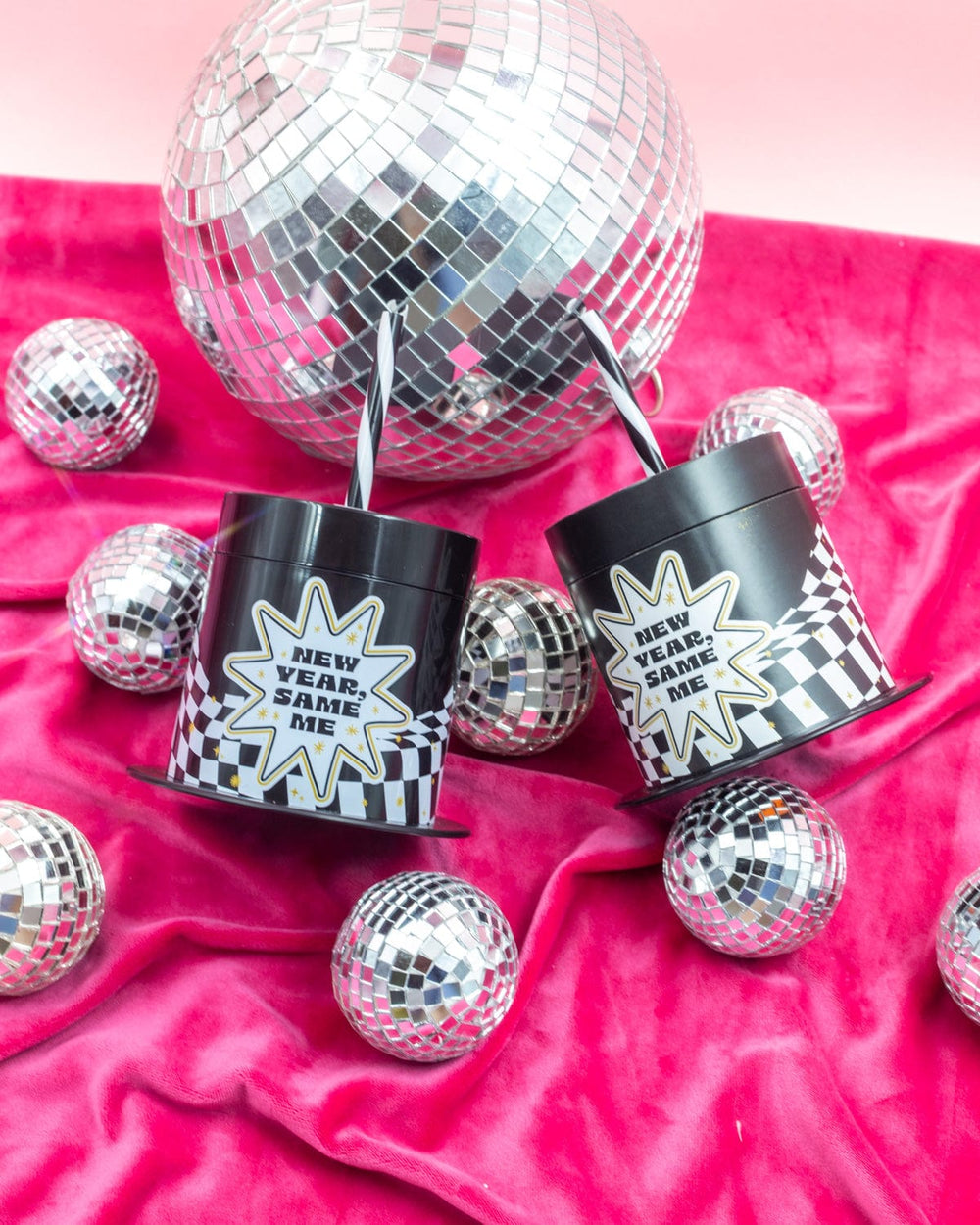 Two New Year, Same Me top hat cups beside a large mirror ball on pink velvet