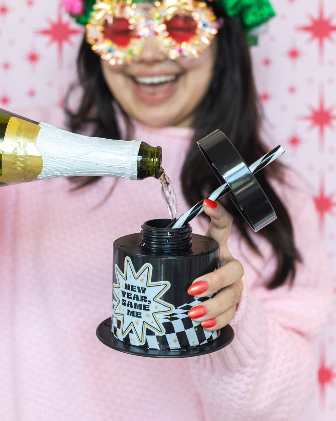 Woman in sparkly glasses pouring champagne into a New Year, Same Me top hat cup
