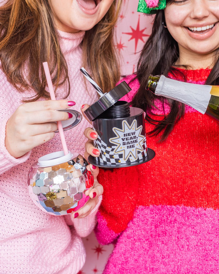 Two friends pouring champagne into a top hat cup and a disco ball cup at a New Year's party
