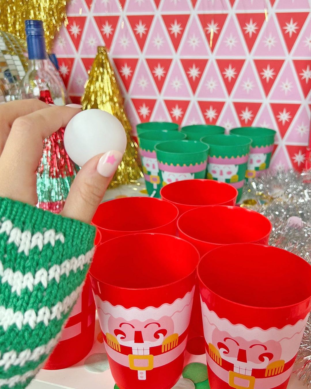 Hand holding a pong ball above red and green nutcracker cups set up for a Christmas party game