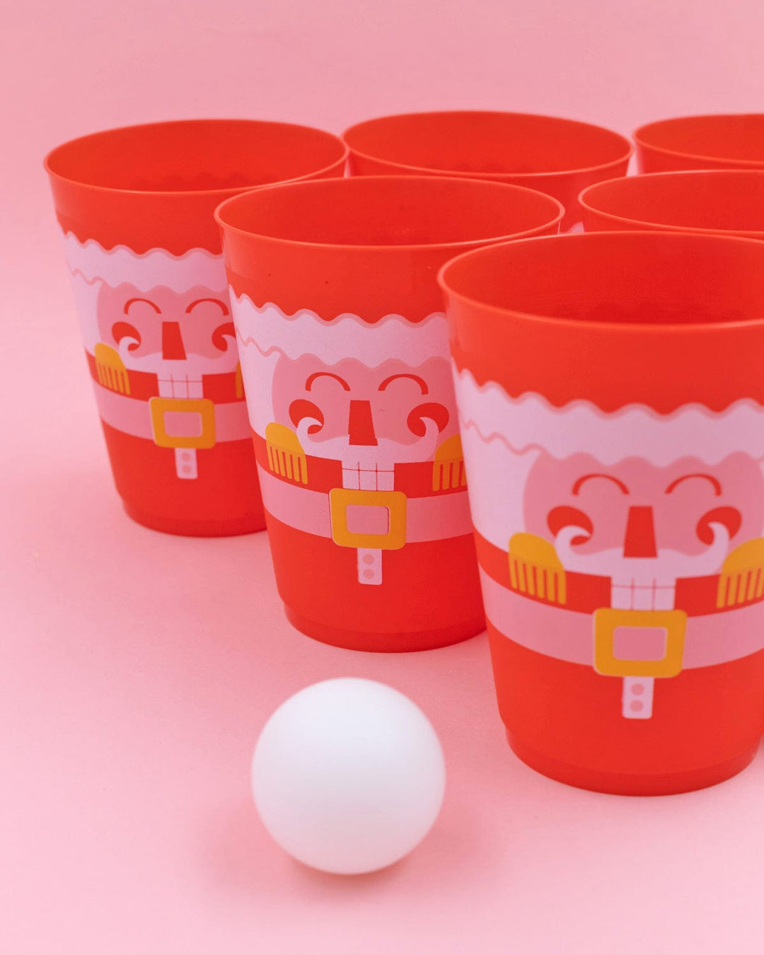 Close-up of a red nutcracker pong cup and ping pong ball on a pink background