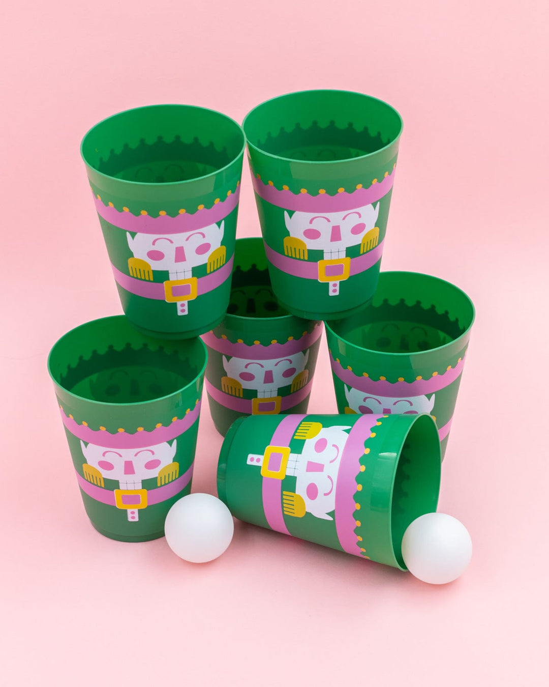Close-up of a green nutcracker pong cup and ping pong balls on a pink background