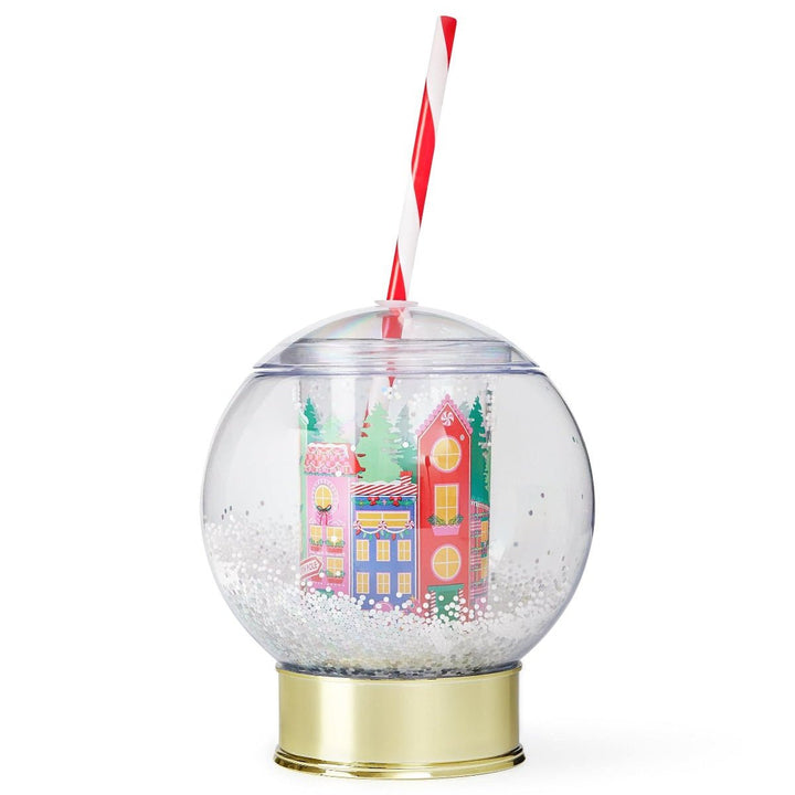 Holiday village snow globe cup with a gold base, snow confetti, and a red and white striped straw