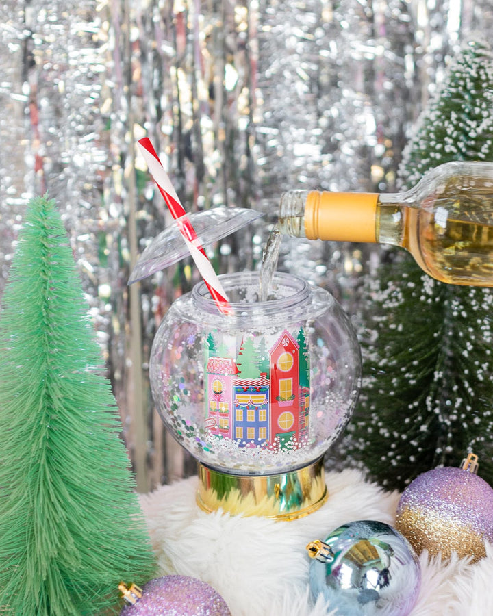 Snow globe sipper filled from a bottle beside green bottle brush trees and silver tinsel