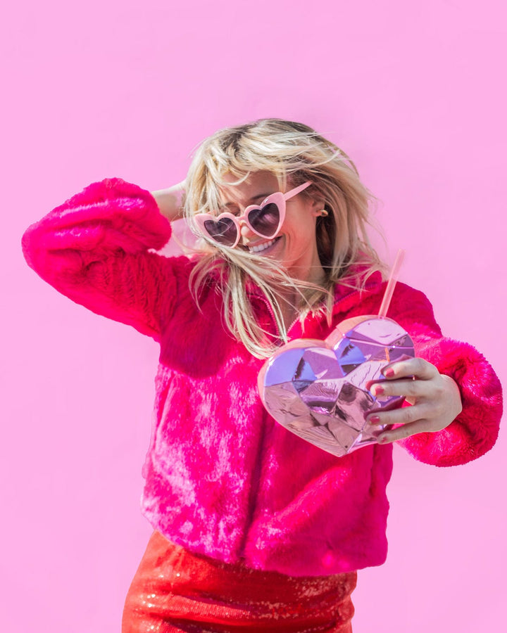 Woman in a pink sequin jacket and heart sunglasses holding a pink heart sipper cup