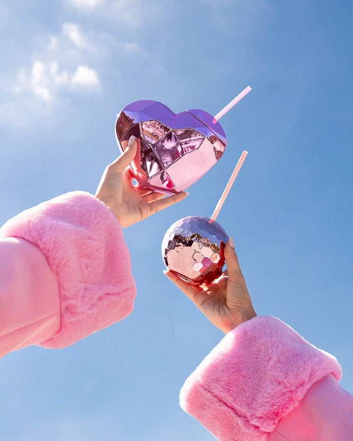 Two hands in pink faux fur cuffs raising a pink heart cup and a disco ball cup to a blue sky