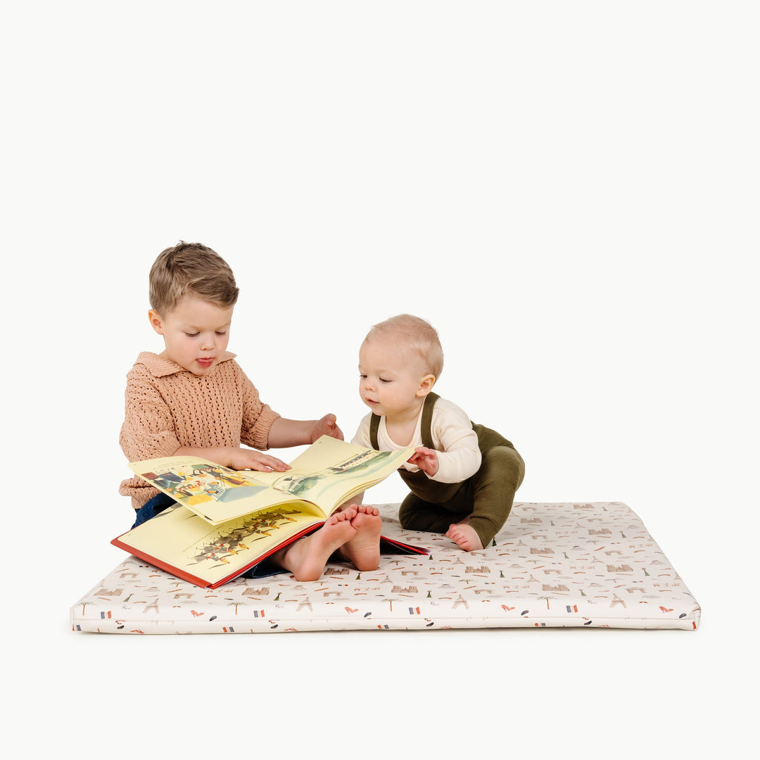 Two children reading a book together on the square Paris print padded play mat