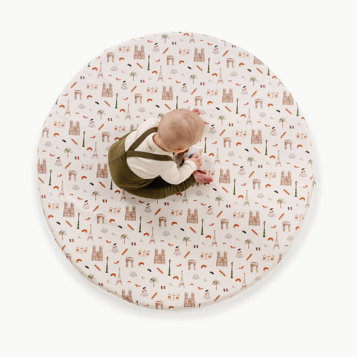Overhead view of a baby playing on the round Paris print padded play mat with Eiffel Tower and cafe motifs