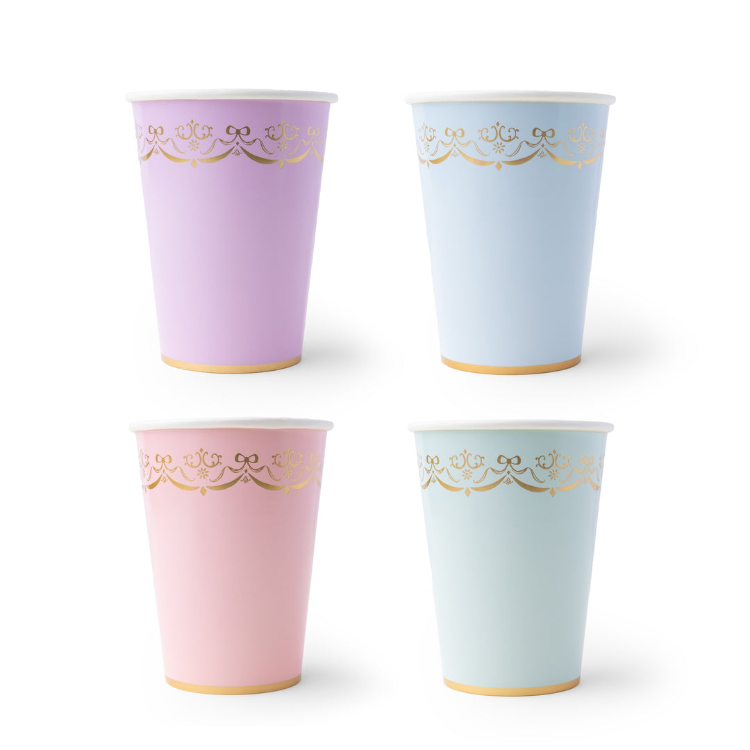 Pastel party cups on a white background, featuring a light pink cup in the front with a gold decorative border and a gold base, with other cups in blue, purple, and white stacked behind it.