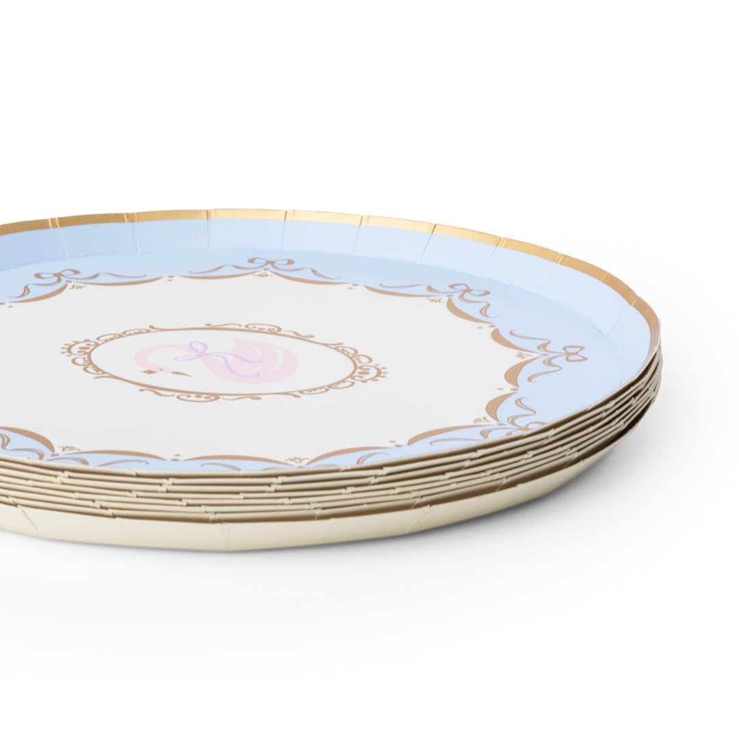 A stack of round paper plates with a light blue outer ring, a white center, gold decorative border details, and a small pink monogram design in the middle, shown on a white background.
