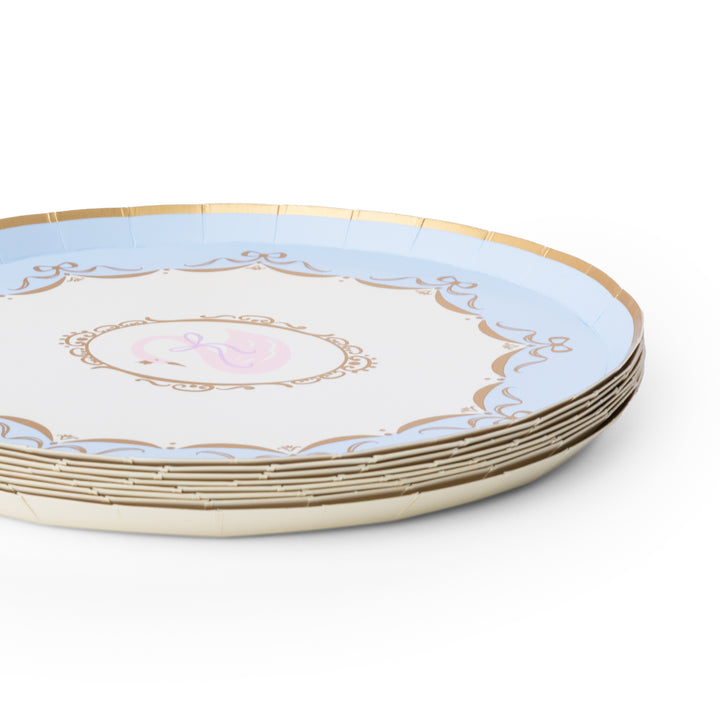A stack of round paper plates with a light blue outer ring, a white center, gold decorative border details, and a small pink monogram design in the middle, shown on a white background.